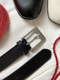 Musta nahkavyö, jossa on hopeanvärinen metallisolki, sileä pinta ja suorakulmainen muoto, sijoitettuna erilaisten asusteiden viereen.