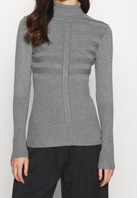 Pull à col roulé gris à manches longues avec texture côtelée aux poignets et sur la partie inférieure, présentant un motif rayé horizontal sur la poitrine.