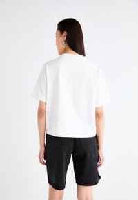 T-shirt blanche à manches courtes avec une coupe droite, associée à un short en denim noir avec des poches arrière et une coupe décontractée.