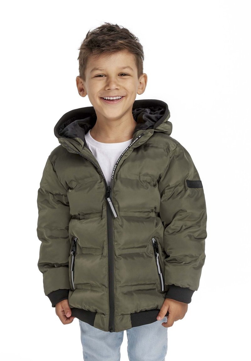 Puffjacka i olivgrönt, med en quiltad design, dragkedjefickor och en svart huva. Buren över en vit skjorta och denimjeans.