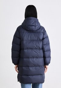 Marinblå pufferjacka med huva, med en kviltad design, elastiska manschetter och lång längd. Slät yta och varm isolering.