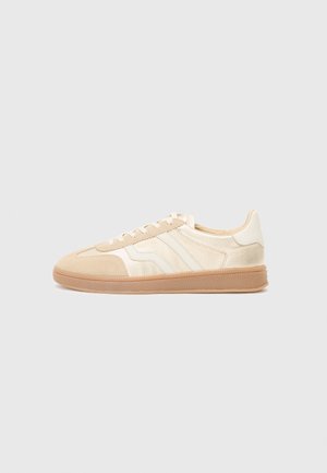Sneakers met een beige bovenkant van suède en gladde texturen. Drie witte strepen langs de zijkant en een rubberen gum zool.