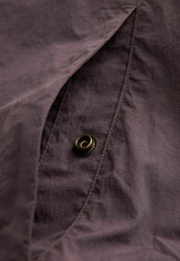 Material texturat de culoare maro, cu un model subtil de tip grilă, dotat cu un nasture metallic auriu și cusături în contrast pe margine.