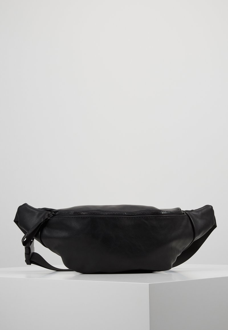 Banane en cuir noir avec fermeture éclair et sangle réglable, présentée sur un socle blanc sur fond uni.