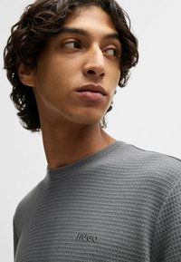 Grått strukturerat T-shirt med rund halsringning och subtil HUGO-logga. Tyget är vävt i ett rutmönster som skapar djup.