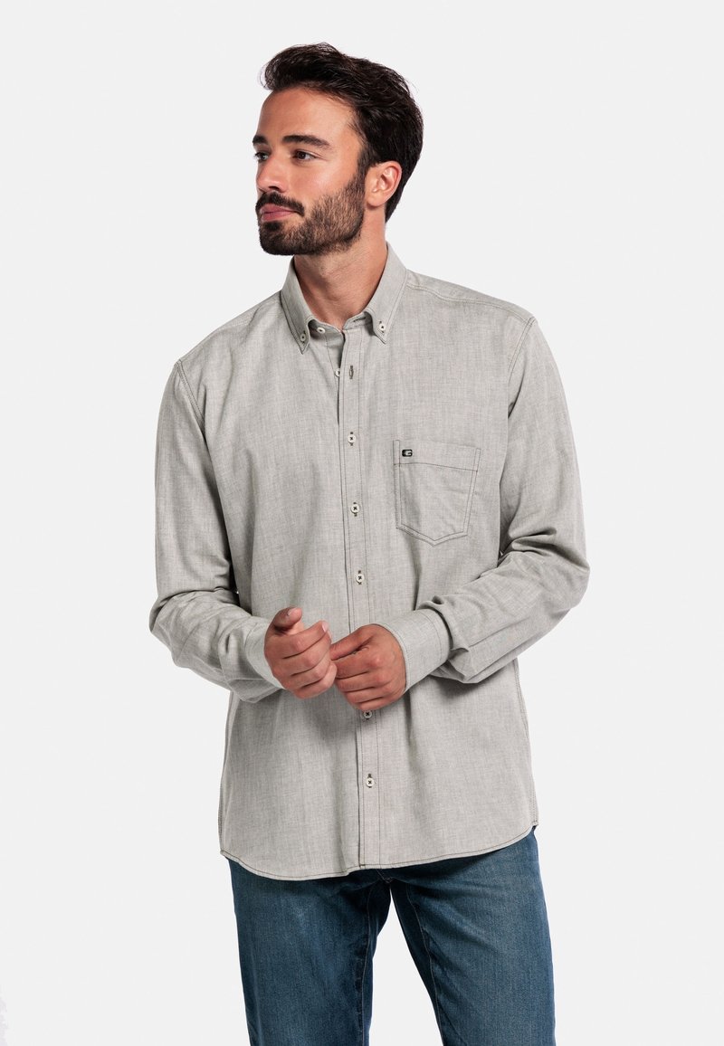 Lichtgrijze overhemden met een gestructureerde stof, voorzien van een enkele borstzak en een puntige kraag, gecombineerd met blauwe spijkerbroek, staand model.