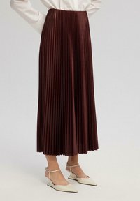 Gonna plissettata bordeaux con un alto punto vita, design fluido e texture lucida, abbinata a scarpe con zeppa bianche con cinturini alla caviglia.