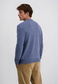 Strukturierter, blauer Strickpullover mit Rundhalsausschnitt und geripptem Saum, kombiniert mit stofflichen Hosen in einem beigen Farbton, von hinten gezeigt.