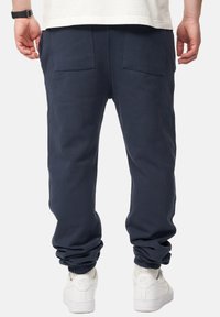 Marinefarbene Jogginghosen aus Baumwollmischung, mit elastischen Bündchen, zwei Gesäßtaschen und lockerem Schnitt. Kombiniert mit weißen Sneakers.