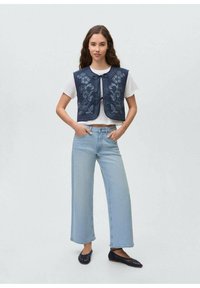 Mornarsko modro floralno vezeno telovnik s okroglim izrezom, oblečen preko bele majice, kombiniran s svetlo modrimi širokimi hlačami in temnimi balerinkami.