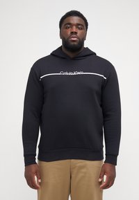 Zwarte hoodie van een katoenmix, met een witte horizontale streep en het "Calvin Klein" logo op de borst, geribbelde manchetten en onderkant.
