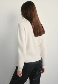 Prążkowany biały sweter z długimi rękawami, dopasowany krój i okrągły dekolt, w połączeniu z czarnymi skórzanymi spodniami, widok z tyłu.