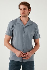 Polo de manga corta en azul pizarra, con cuello a rayas, botón frontal y tela texturizada. Llevado con unos vaqueros informales.