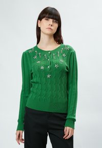 Grüner Kabelstrickpullover mit langen Ärmeln, verziert mit floralen Akzenten und einem runden Ausschnitt. Das Material ist strukturiert und hat gerippte Bündchen.