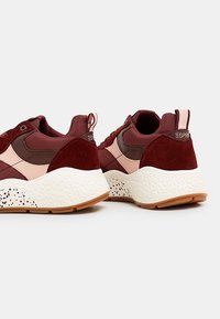 Baskets bordeaux en mesh et suède, avec une semelle blanche texturée parsemée de taches noires et un accent rose.