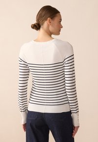 Pull en tricot rayé blanc et marine, avec un col rond, des manches longues et des poignets côtelés ornés de boutons.