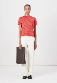 Red patterned short-sleeve t-shirt paired with cream wide-leg pants and a brown leather tote bag, standing on a neutral background.