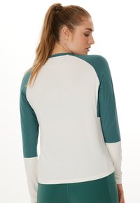 Langærmet atletisk top med farveblokeret design i teal og off-white paneler, glat tekstur og rund halsudskæring.
