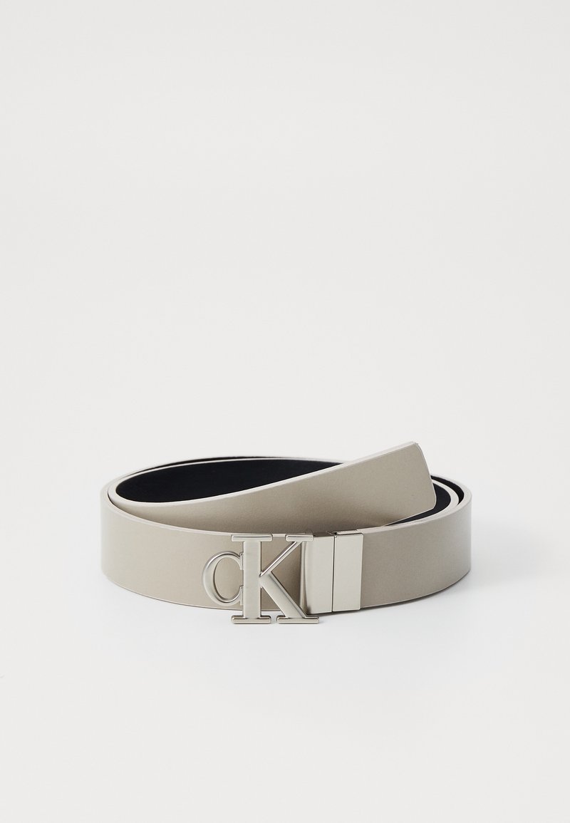 Beige leren riem met een gladde textuur en een gepolijste zilveren logo-sluiter met "CK." Het ontwerp is minimalistisch en gestroomlijnd.