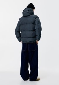 Padded dark gray jacket with a hood, featuring a quilted design. Worn with loose-fitting dark denim jeans and beige shoes.