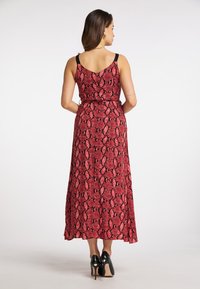 Robe maxi imprimée serpent rouge avec un corsage ajusté, des bretelles noires réglables et un ourlet fluide. Assortie à des talons noirs pour le style.