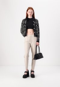 Čierno-biela károvaná skrátená bunda, čierny crop top, béžové upravené nohavice, čierne platformové topánky a malá čierna kabelka.