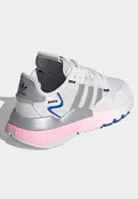 Białe buty sportowe z szarymi akcentami, teksturowana siateczka na górze, trzy srebrne paski, różowa i niebieska piankowa podeszwa oraz odblaskowe detale z tyłu.