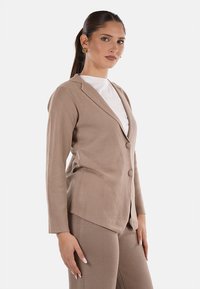 Blazer su misura beige made of soft fabric, con colletto a faccia, due pulsanti, maniche lunghe e orlo obliquo. Texture liscia, design minimalista.