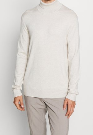 Pull en fil doux à col roulé. Présente un design ajusté, des poignets côtelés et une texture lisse. Porté avec un pantalon beige.