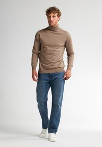 Un pull col roulé marron au design ajusté associé à un jean bleu. La tenue est complétée par des baskets blanches. Texture lisse tout au long.