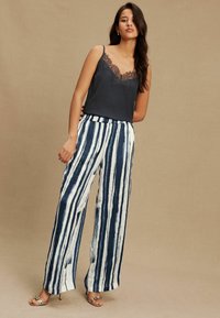 Black lace-trimmed camisole paired with white pants featuring navy vertical stripes, designed with a relaxed fit and wide leg silhouette.