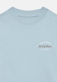 Ανοιχτό μπλε βαμβακερό t-shirt με στρογγυλή λαιμόκοψη και τυπωμένο λογότυπο σε λευκό και σκούρο μπλε στο αριστερό στήθος. Ομαλή υφή, casual σχεδιασμός.