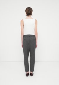 Top blanco sin mangas combinado con pantalones grises de textura, con un corte relajado y una cintura elástica. La modelo lleva zapatos burdeos.