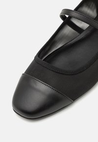 Black flats made of textile and leather, featuring a round toe, elastic strap, and textured fabric along the upper section.