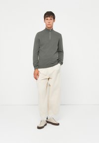 Grå genser med glidelås og lange ermer, kombinert med løstsittende kremfargede bukser og beige sneakers. Minimalistisk design, ensfargede teksturer.