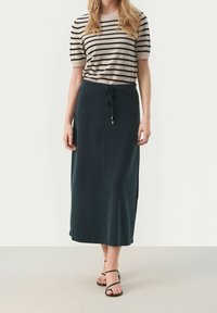 Haut à rayures à manches courtes en beige et noir associé à une longue jupe teal foncé. La jupe possède une taille à cordon de serrage et une texture lisse.