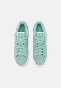 Light green suede sneakers with a lace-up design, white rubber sole, and Adidas branding on the tongue and side. Clean, minimalistic look.