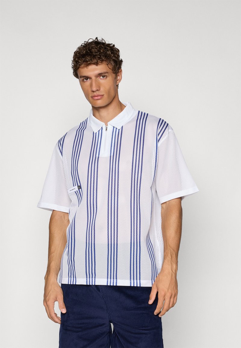 Hvit mesh polo skjorte med blå vertikale striper, korte ermer og krage med glidelås. Har en subtil merkeetikett på siden.
