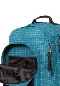 Tealfärgad ryggsäck med ett rutmönster och svarta detaljer. Har ett handtag på toppen, flera fack och dragkedjeöglor. Tillverkad av syntetiskt material.