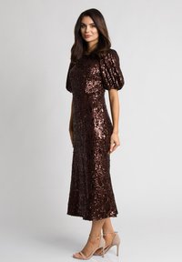 Brązowa sukienka z cekinami, z bufkami, długość do kolan, dopasowany fason. Połączona z cielistymi sandałami na wysokim obcasie. Gładka faktura materiału.