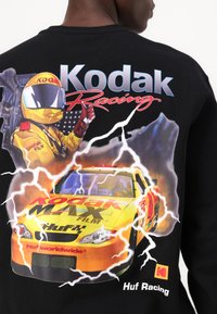 Sort sweatshirt med et grafisk print af en racerbilsfører i en gul uniform, med livlige farver og lynakcenter.