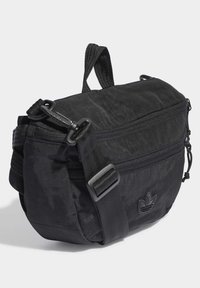 Kompaktní černá crossbody taška s nastavitelným popruhem, dvěma přihrádkami na zip a jemným logem Adidas na předním panelu.