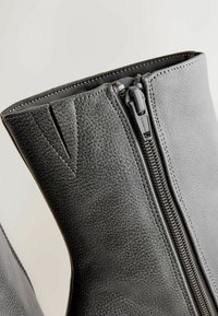 Szare skórzane botki za kostkę charakteryzują się zapięciem na zamek błyskawiczny, teksturowanym materiałem oraz przeszyciami wzdłuż krawędzi, a także gładką podszewką wewnętrzną.