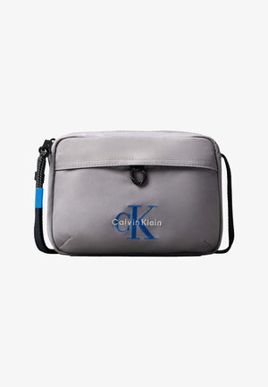 Svetlo siva pravokotna torbica čez ramo s črnim nastavljivim trakom in modrim logotipom "CK Calvin Klein" na sprednjem žepu.
