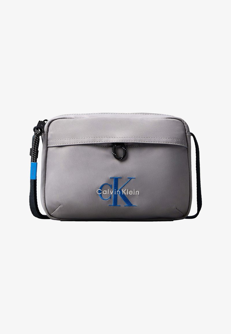 Ανοιχτό γκρι ορθογώνια τσάντα χιαστί με μαύρο ρυθμιζόμενο λουράκι και μπλε λογότυπο "CK Calvin Klein" στην μπροστινή τσέπη.
