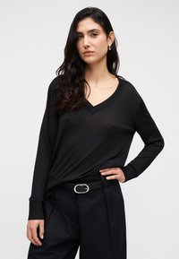 Pull noir à col en V avec manches longues, tissu doux, coupe décontractée, associé à un pantalon taille haute et une ceinture noire avec une boucle argentée.