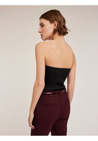Svart ribbad strapless top i kombination med bordeauxfärgade skräddarsydda byxor med ett glansigt bälte. Outfiten visar upp en figursydd silhuett och en slät textur.