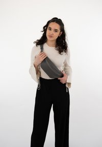Borsa a tracolla grigia realizzata in tessuto liscio con una cerniera diagonale, indossata attraversato il corpo; abbinata a un maglione leggero e pantaloni neri plissettati.