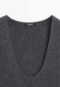 Haut en tricot gris avec un décolleté en V profond. Présente une texture subtile et des détails de couture. Étiquette logo présente au niveau du décolleté.