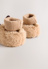 Botines beige con puño de punto y forro suave de piel sintética. Presentan una forma redondeada y tejido texturizado para proporcionar calidez y comodidad.